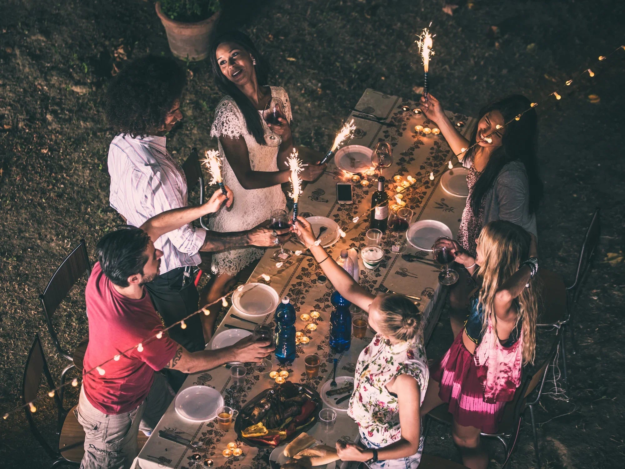 Outdoor backyard BBQ dinner party with friends holding sparklers around a decorated table