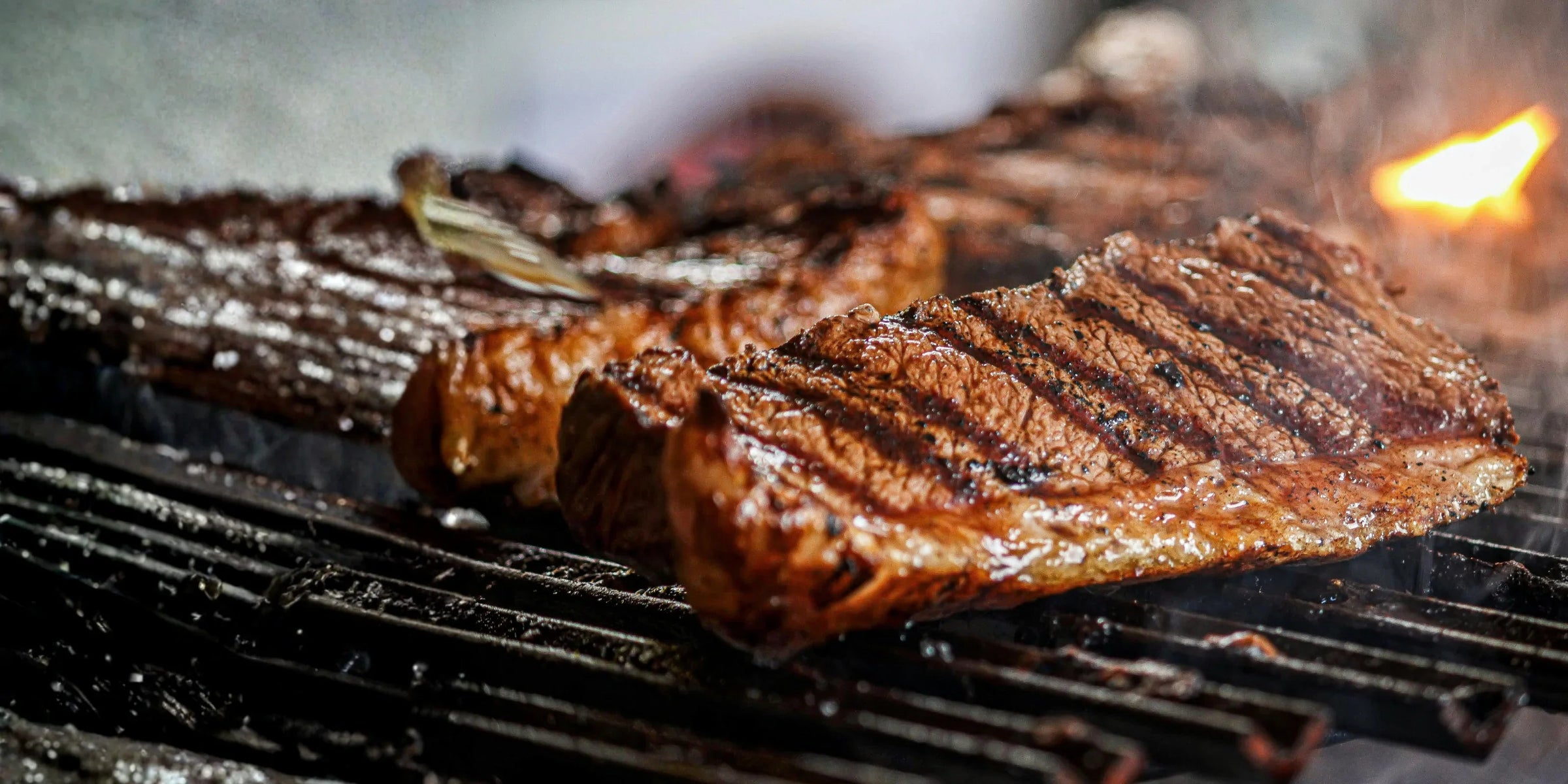 Juicy steak with grill marks sizzling on a barbecue grill with flames and smoke